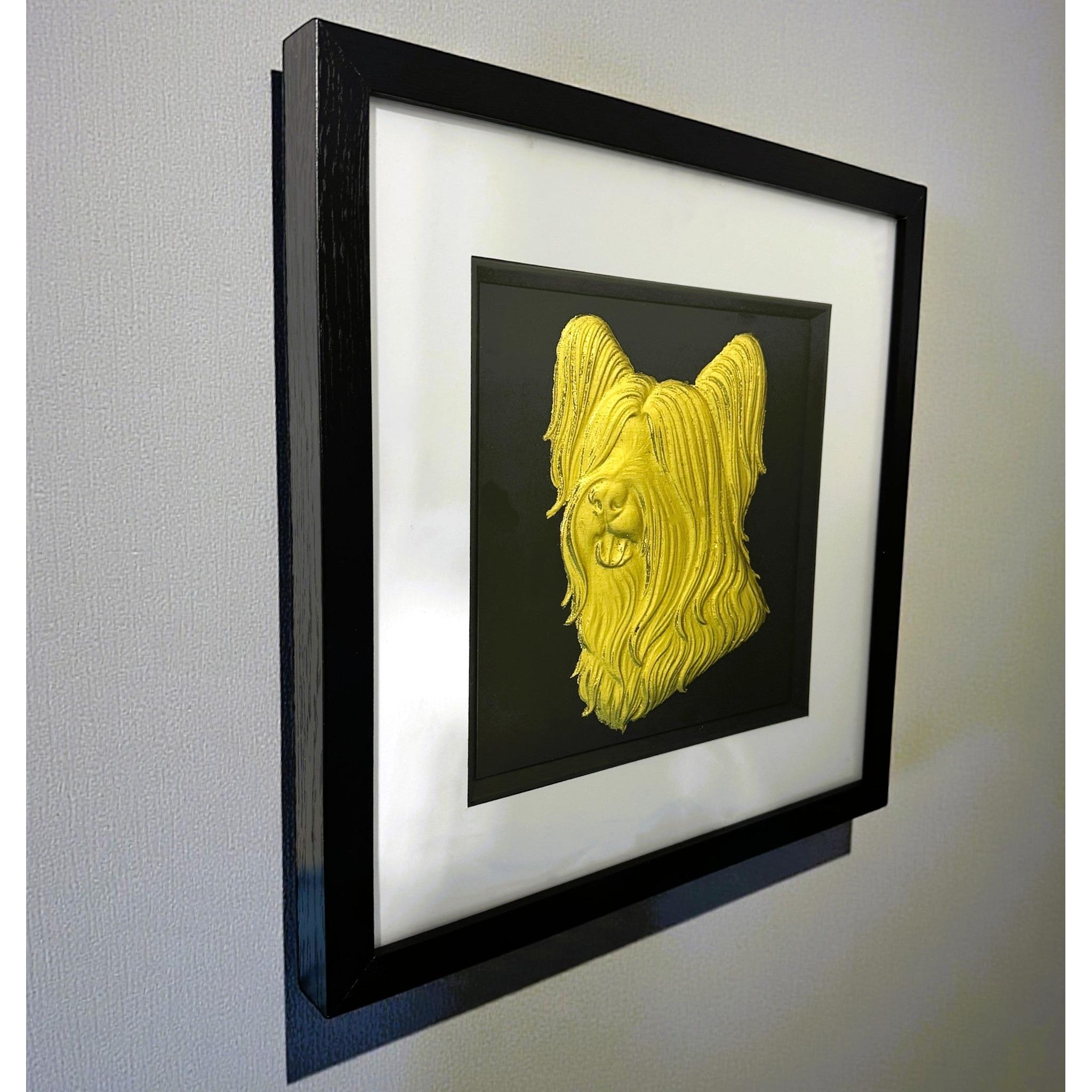 Skye Terrier framed wall art in gold leaf shown mounted on a wall at a slight angle with black wooden frame and white mount