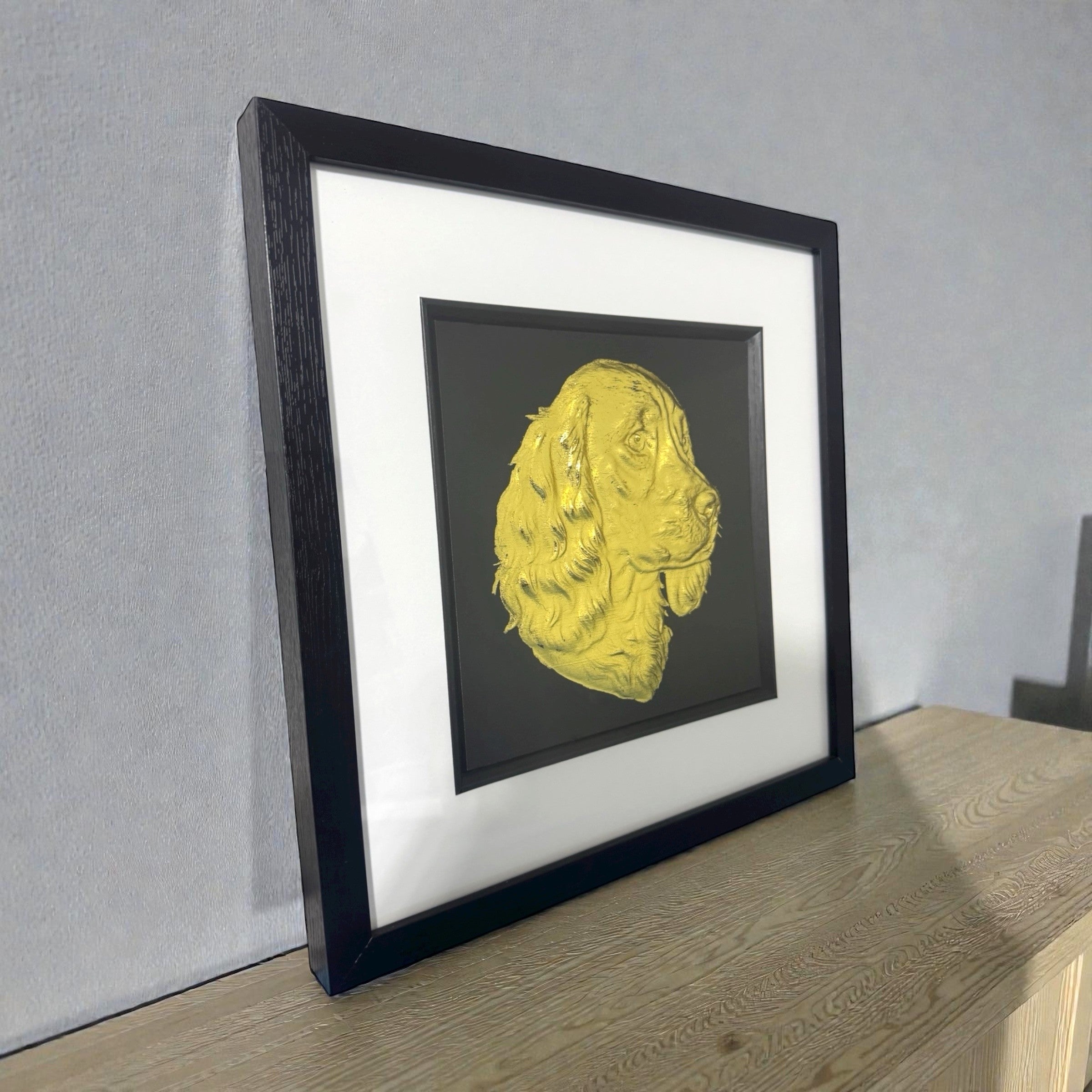 Springer Spaniel gold leaf wall art photographed at an angle on a desk with black frame and white mount
