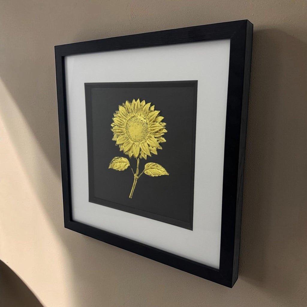 Gold Leaf sunflower relief artwork hung on a neutral wall, angled view showing the depth of the black box frame and white mount