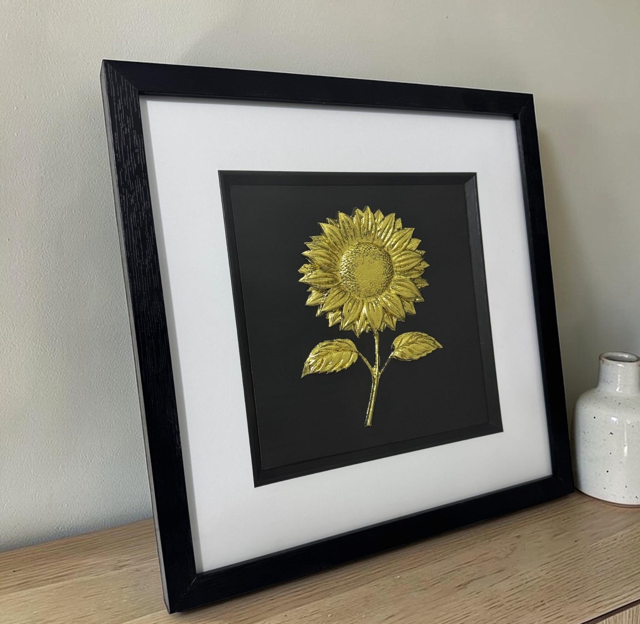 Framed Gold Leaf sunflower relief wall art displayed on a wooden sideboard, black box frame with white mount beside a white ceramic vase
