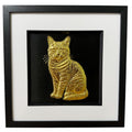 Framed tabby cat wall art, gold relief of a sitting striped tabby, tail curled round its paws, on a black background in a black wooden frame with white mount