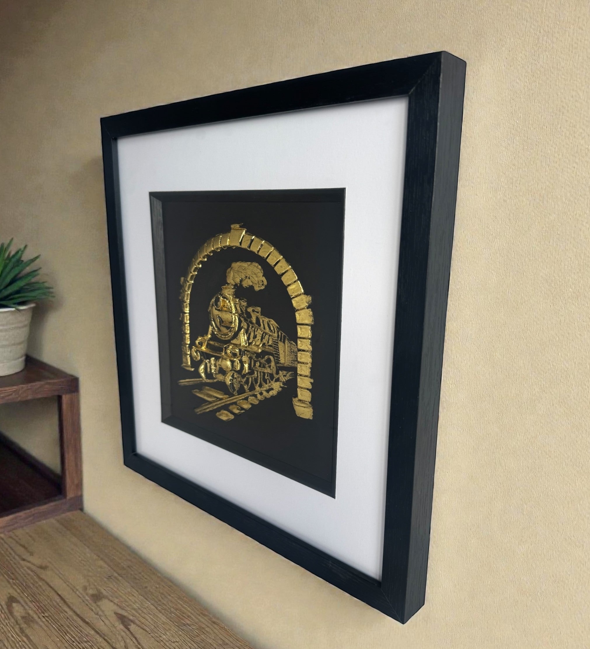 Angled wall view of framed steam locomotive Gold Leaf relief artwork with black box frame, white mount and inner black surround