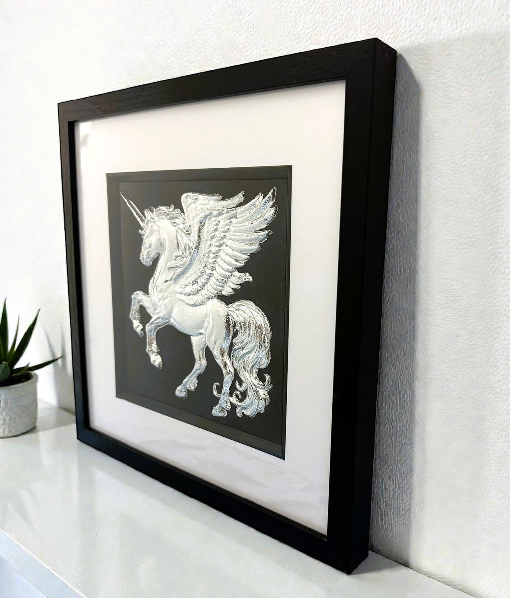 Silver winged unicorn wall art framed in black on a shelf