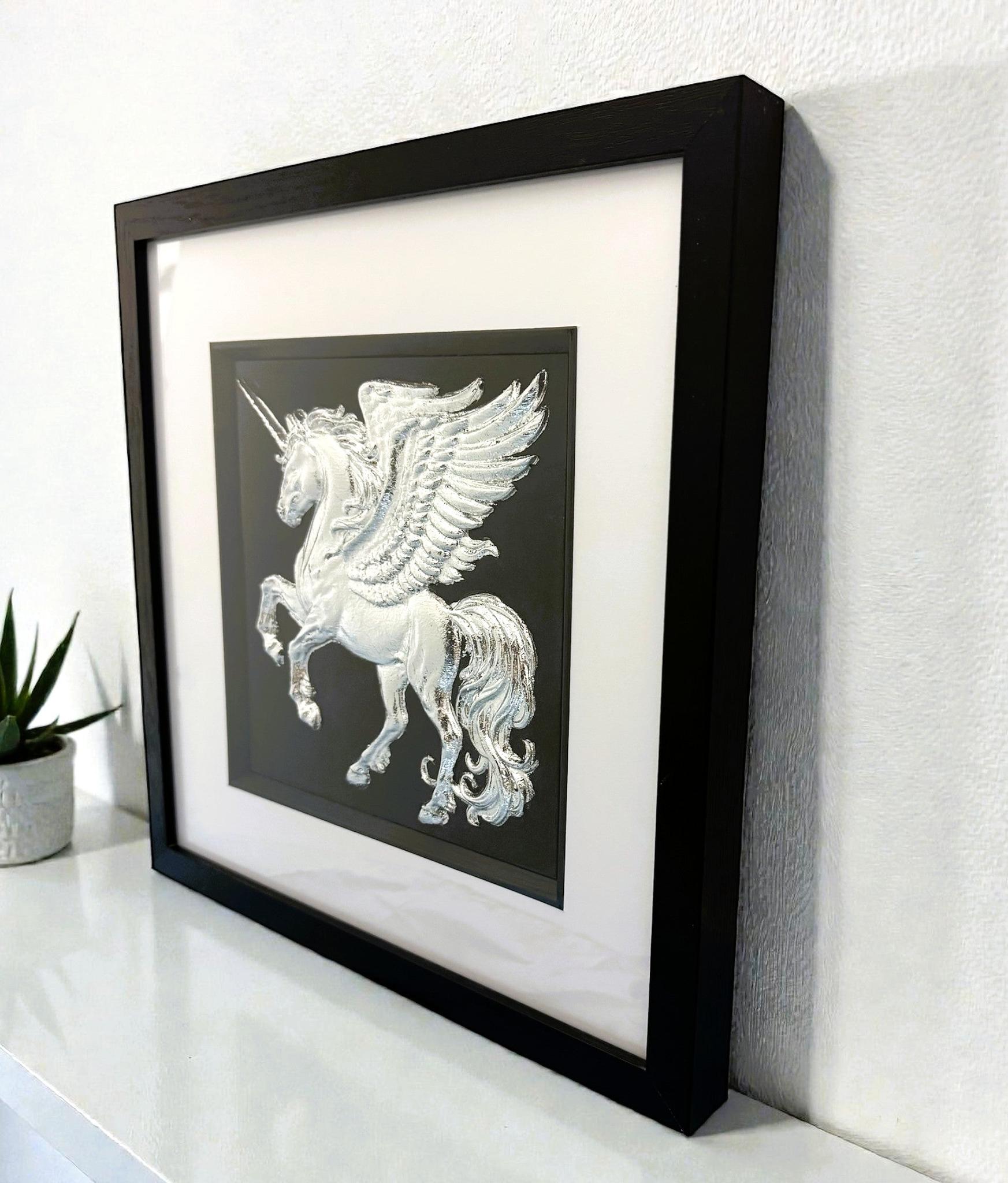 Silver winged unicorn wall art framed in black on a shelf