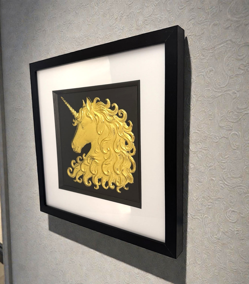 Unicorn wall art in gold leaf mounted on a wall, shown in a black frame with white mount