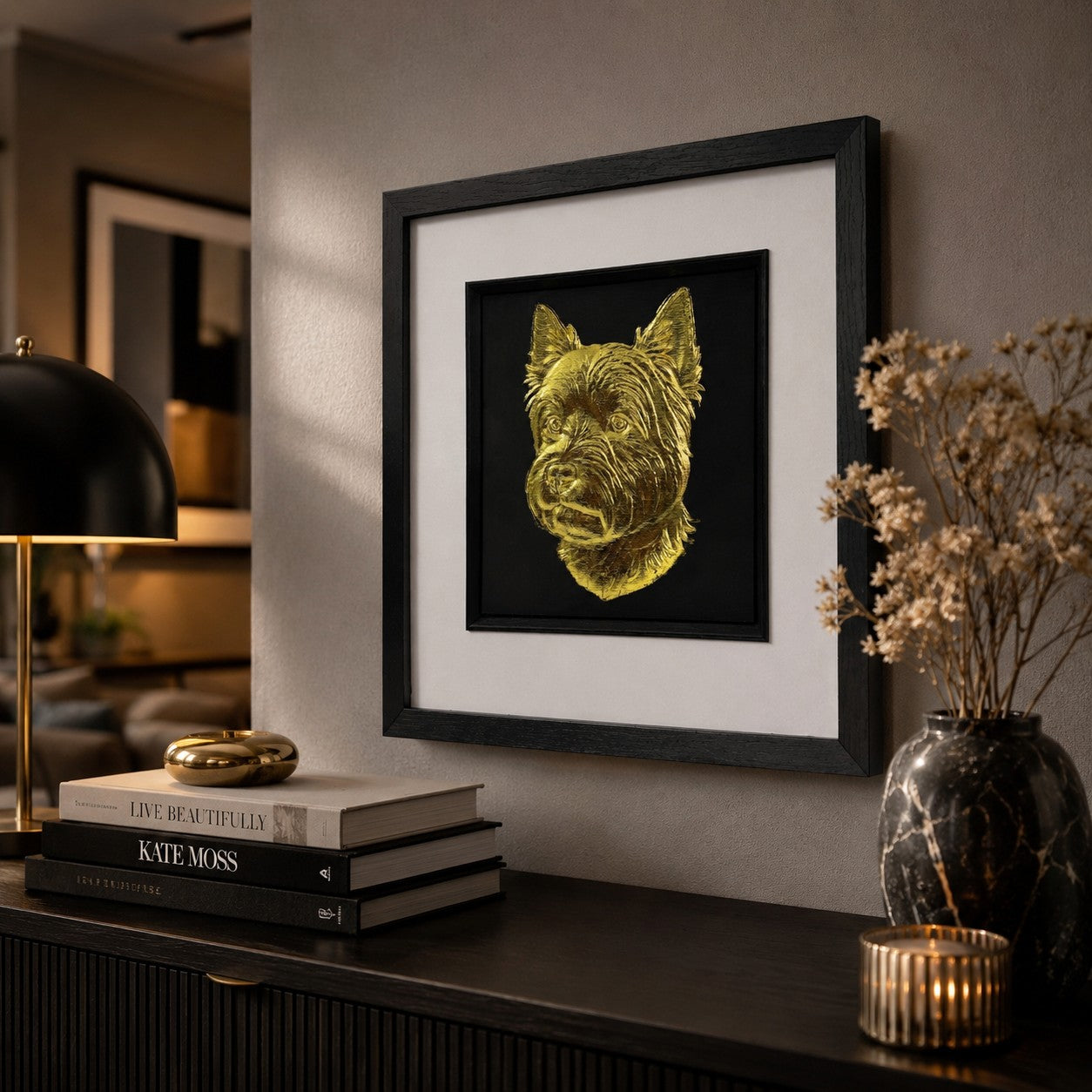 Angled lifestyle view of Westie gold leaf 3D wall art in a black frame, displayed with warm lighting, dark wood, books and luxury brass home decor.