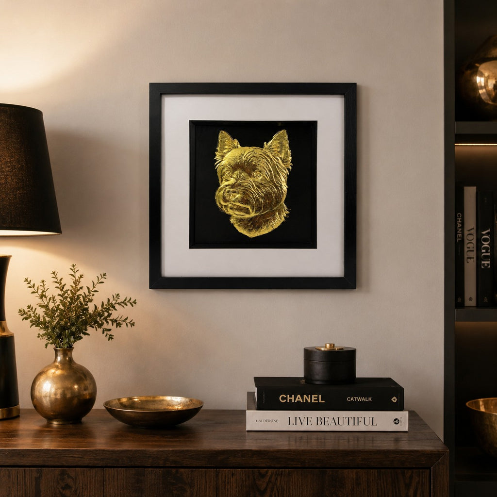 Westie gold leaf 3D wall art in a black square frame, styled on a neutral wall above a wooden sideboard with warm black and brass decor accents.