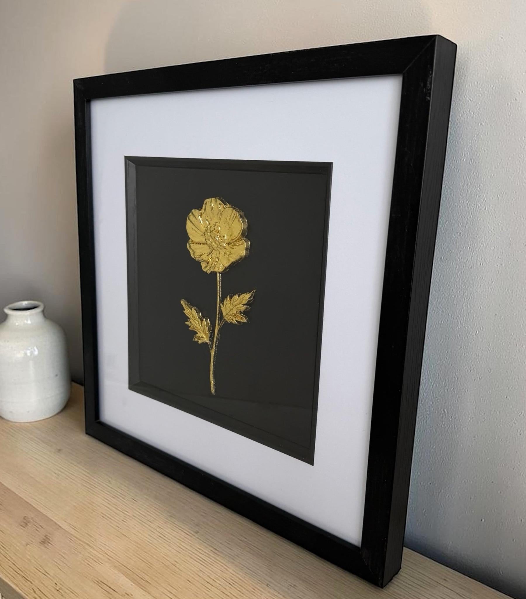 Gold single flower relief artwork in a black frame with white mount, styled beside a small ceramic vase