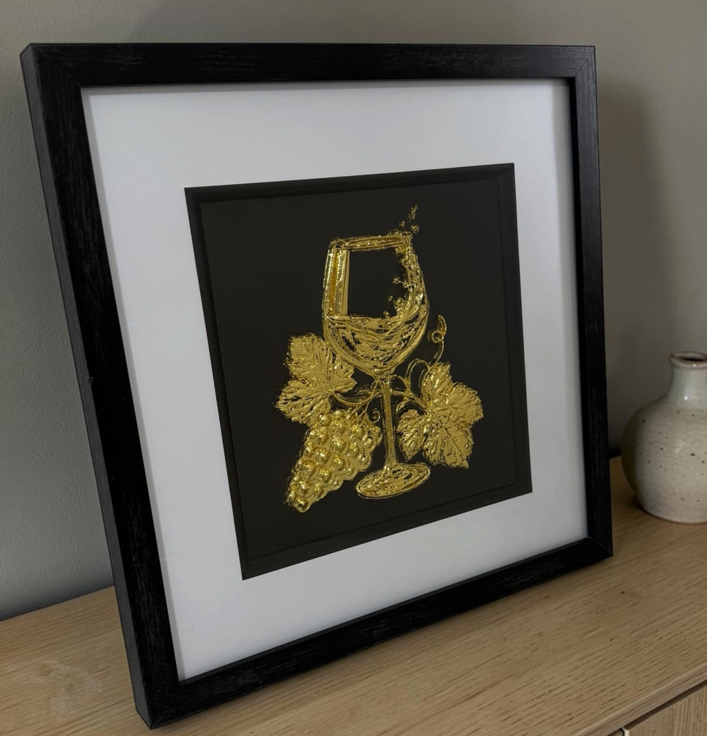 Angled view of gold wine wall art on a sideboard showing black box frame depth and raised detail.